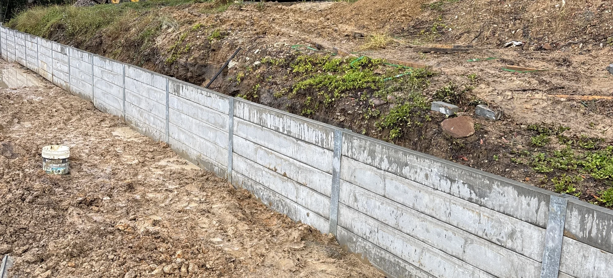 Finished concrete sleeper retaining wall holding back a cut slope