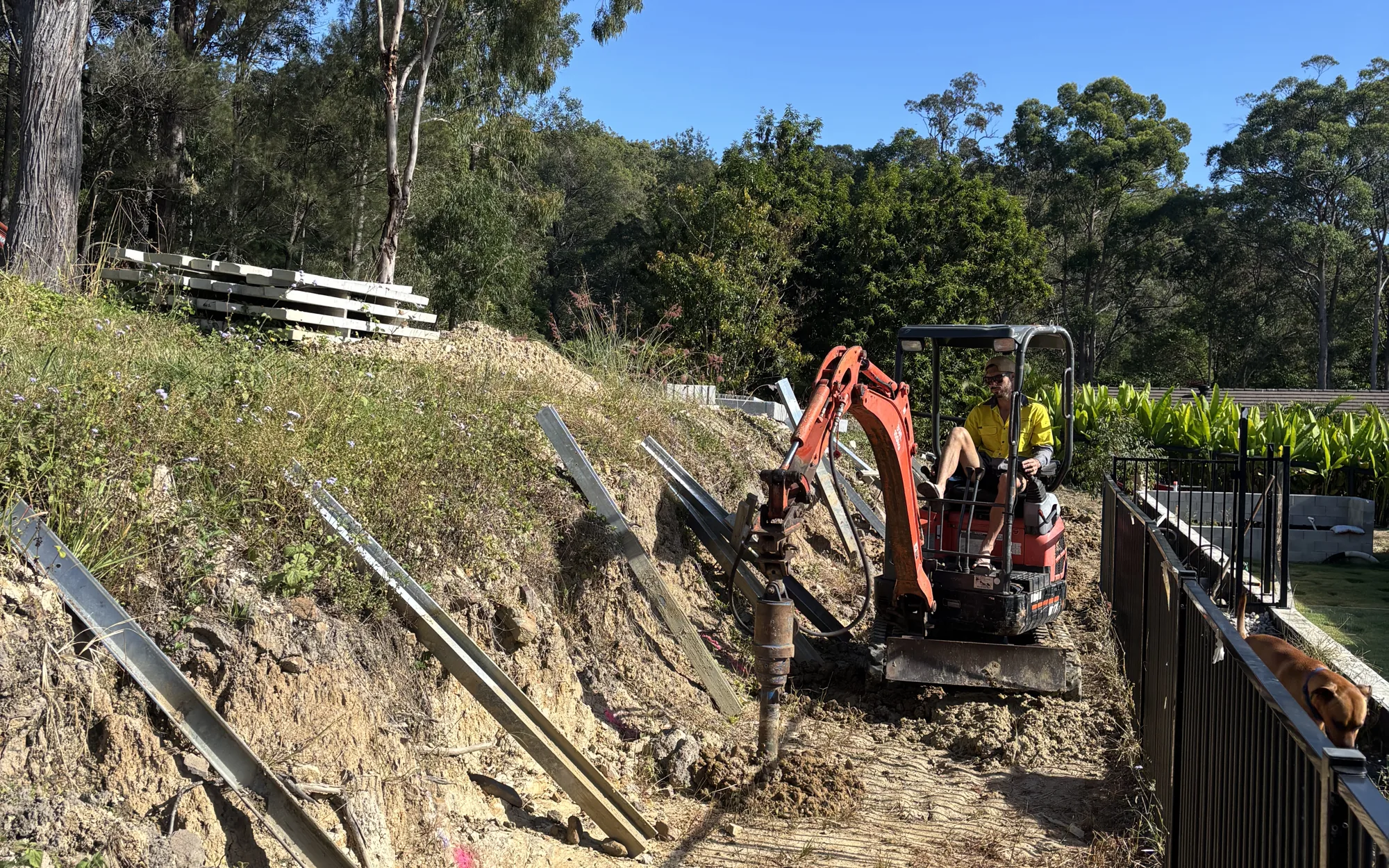 Pro-Form Landscapes setting concrete sleeper retaining wall posts on a sloping Gold Coast block with a mini excavator