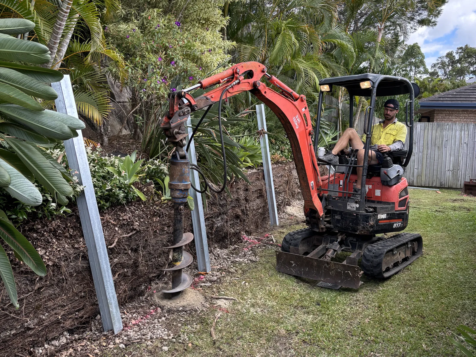 Mini excavator with auger drilling post holes for a concrete sleeper retaining wall